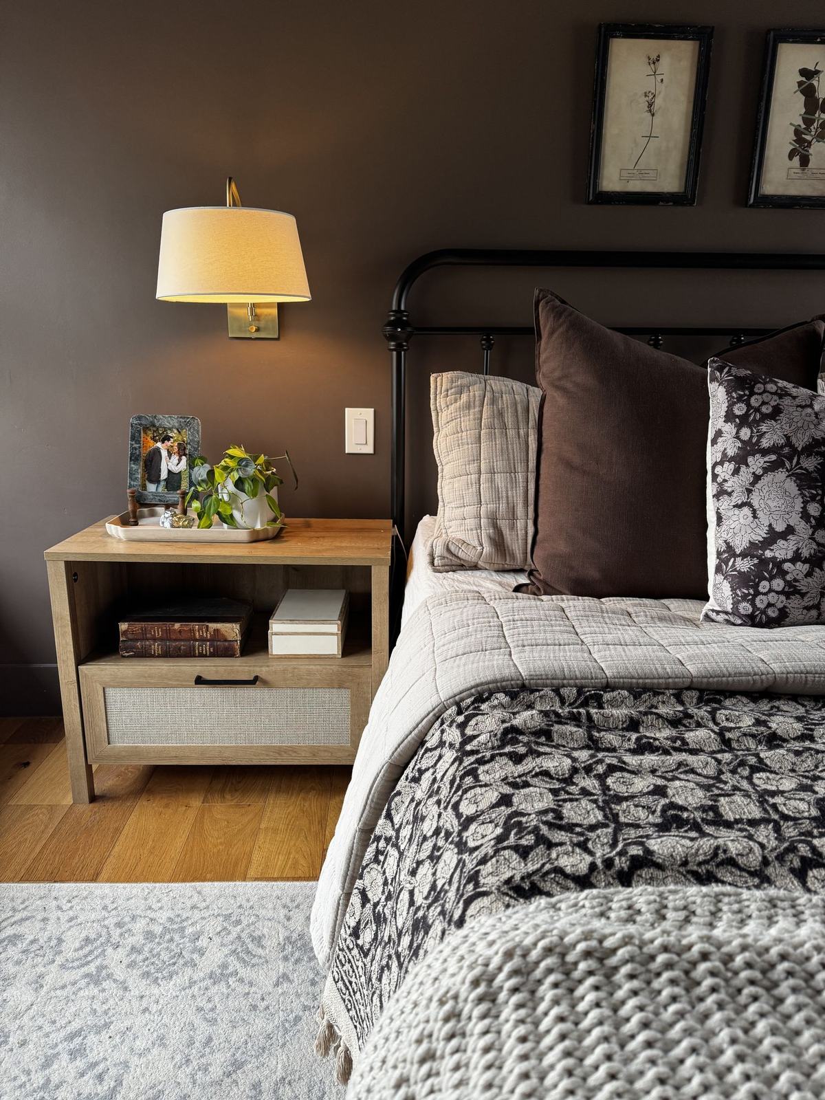 Bedroom with deep brown walls, iron bed frame, layered bedding and brass sconce