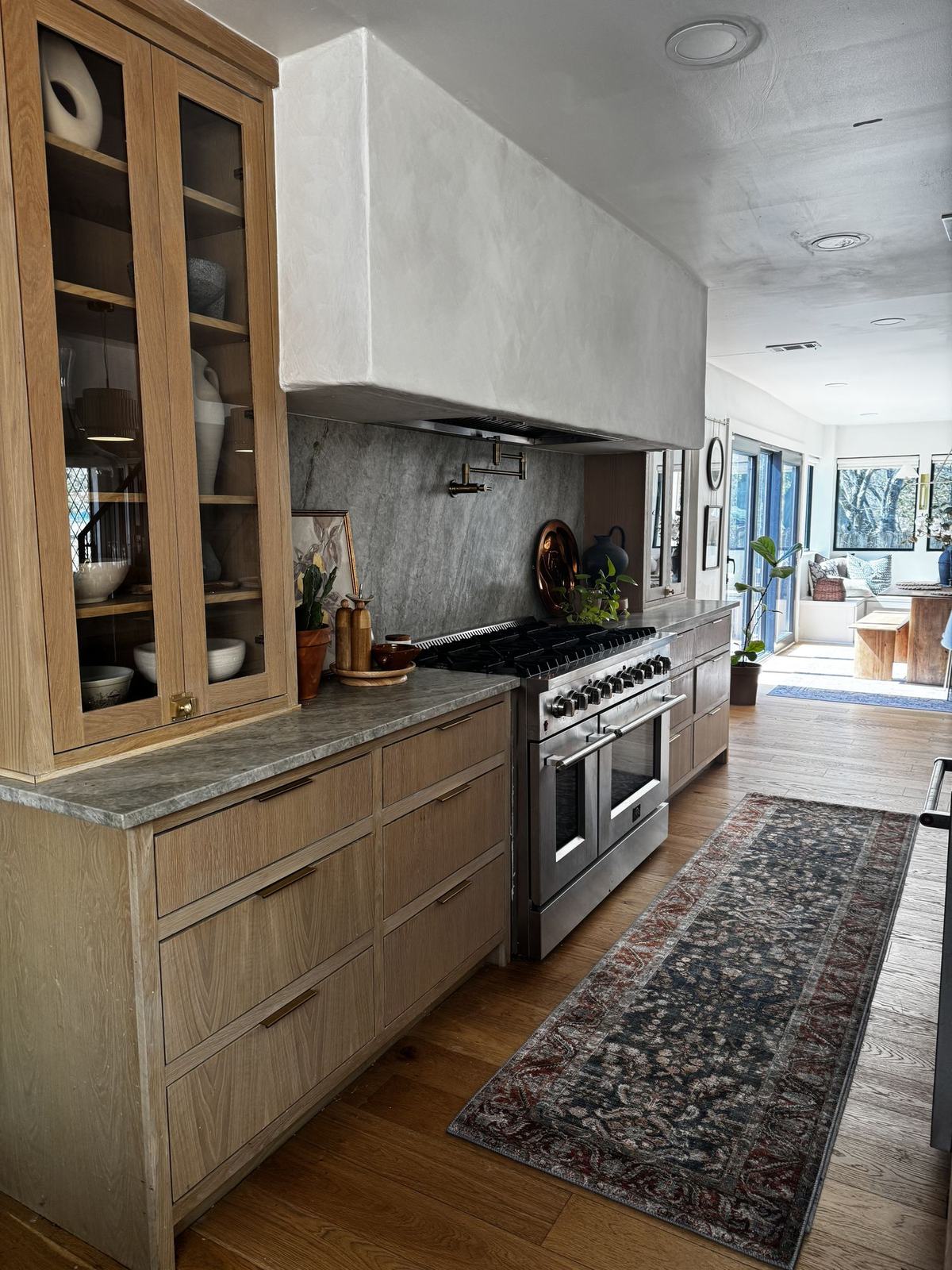 Kitchen with white oak cabinetry, honed stone counters, plaster hood and professional range