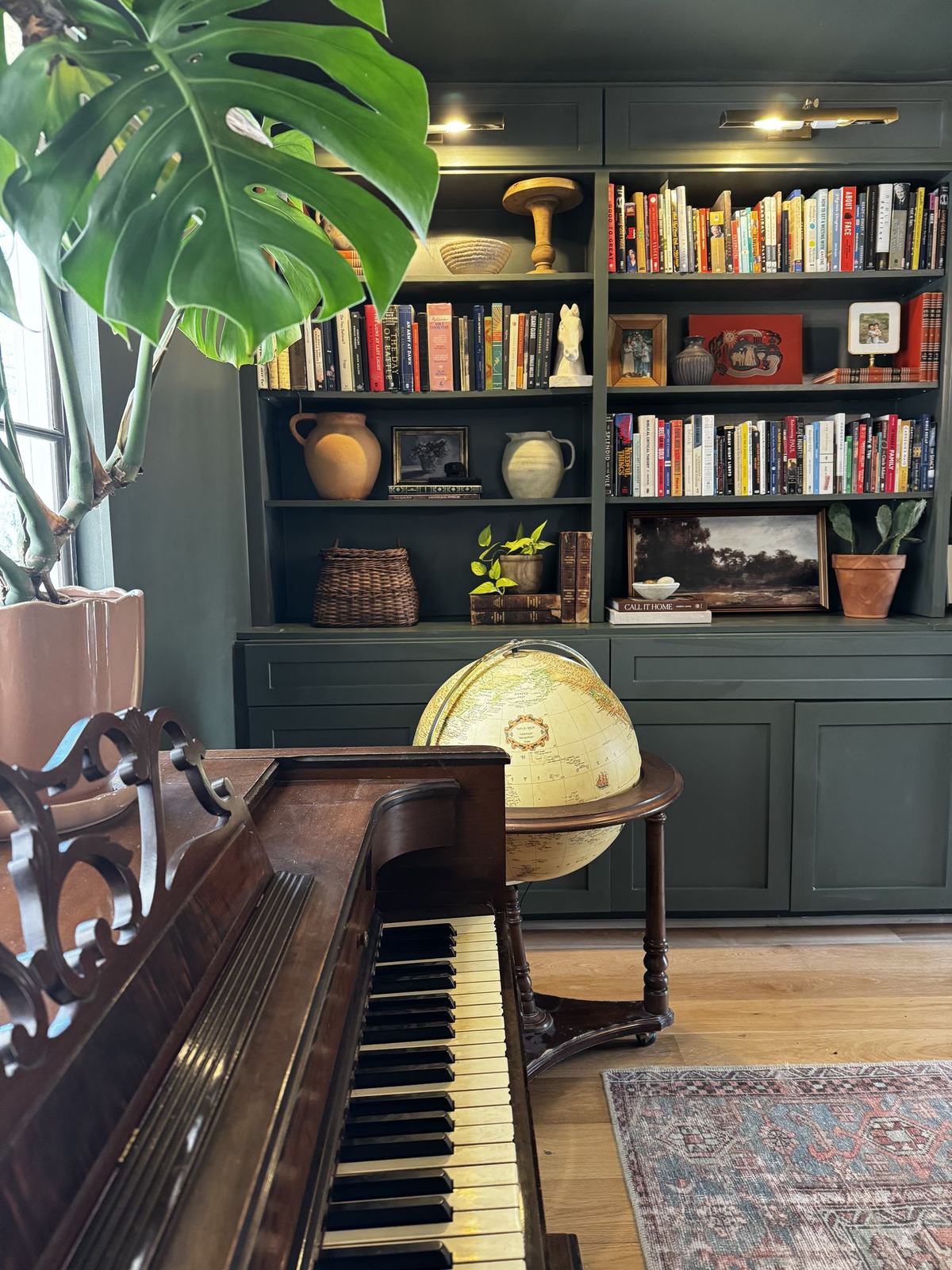 Upright piano beside green built-in shelving filled with books and pottery