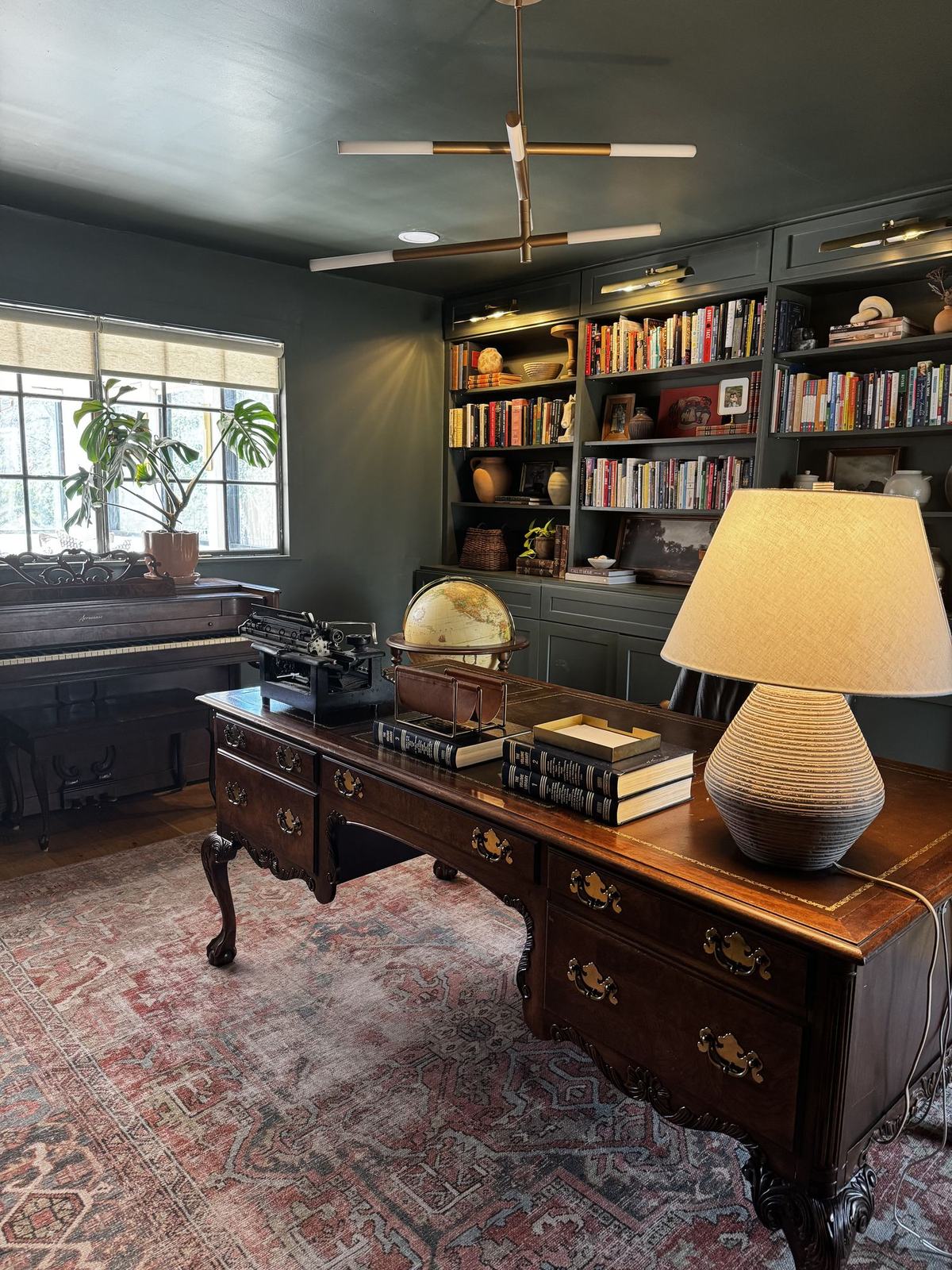 Dark green study with built-in bookshelves, antique desk, and globe